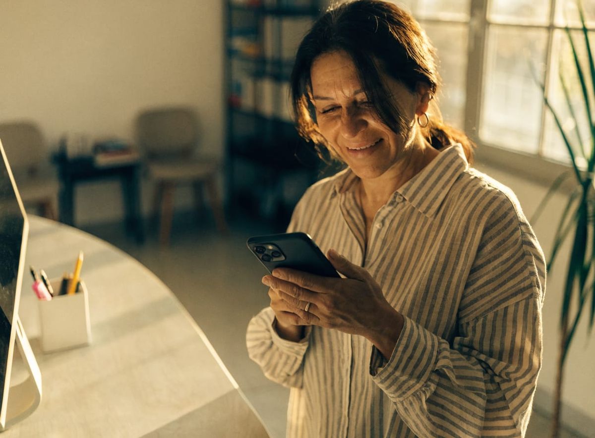 Dueña de un consultorio sonriendo mientras revisa el celular en la recepción