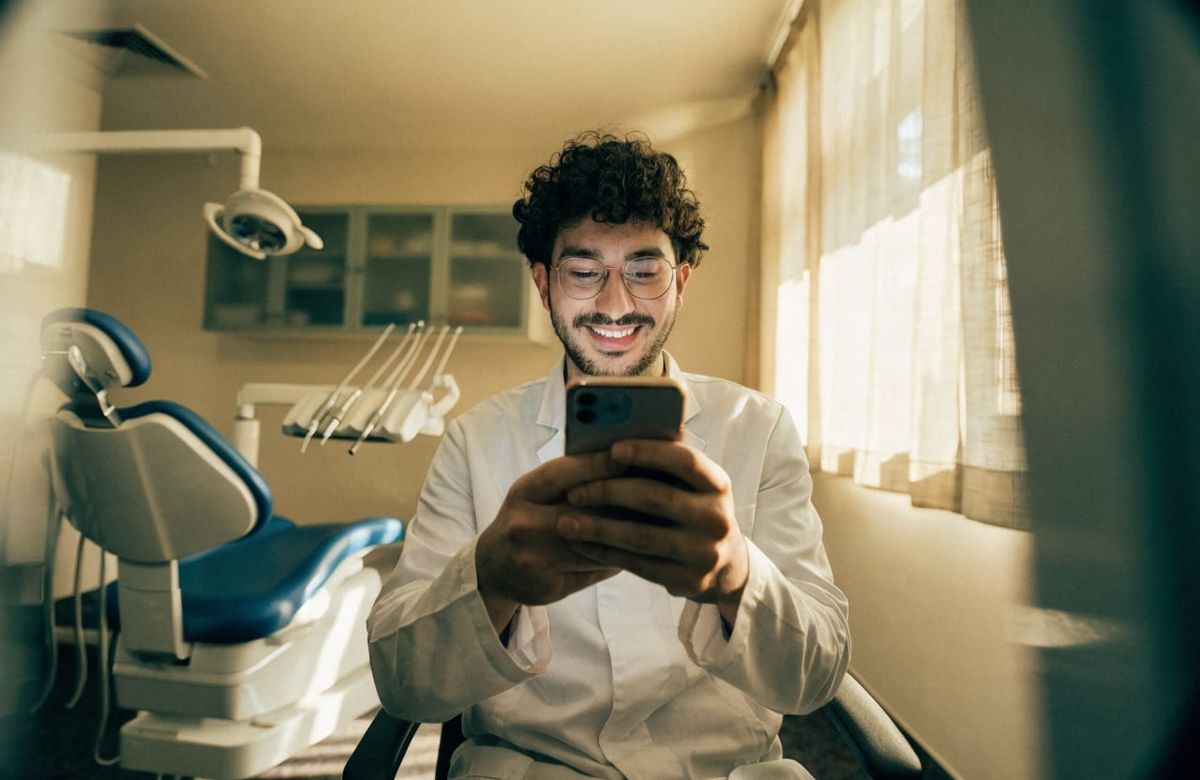 Odontólogo sonriendo mientras usa su celular en el consultorio