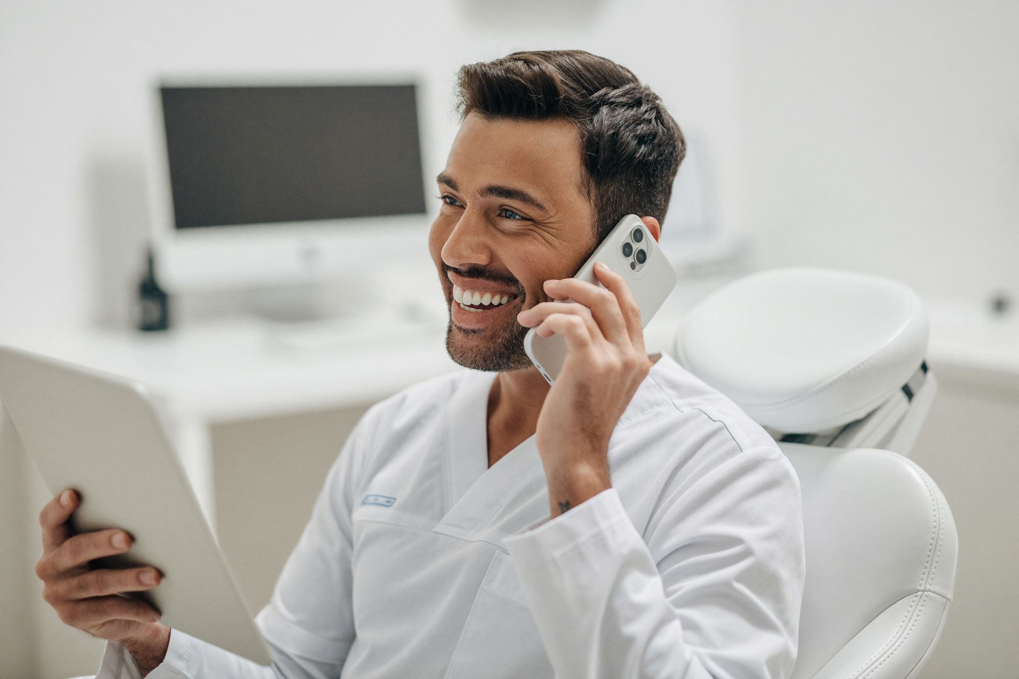 Odontólogo sonriendo mientras habla por teléfono y revisa un recordatorio de WhatsApp en su tablet